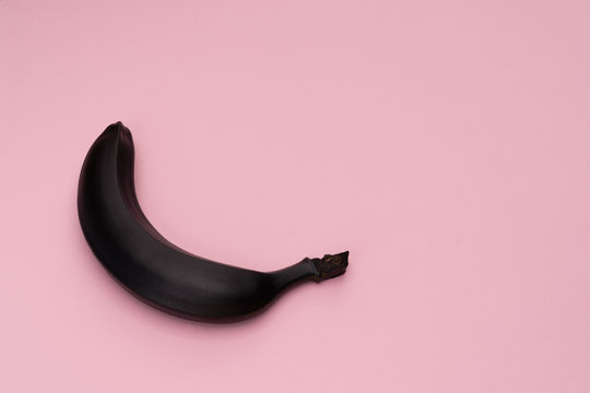 Matte black banana on the pink background. The object is at the left side of the picture. Minimal style. Conceptual minimalism. Matte surface. Fruit. One. Copy space