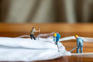 Miniature people : worker team making a homemade mask from white fabric on wood table backgroud