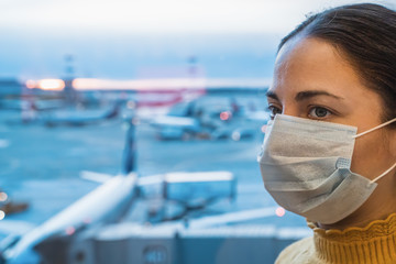 Young woman in anti virus mask in airport terminal at background of airplanes waiting for flight....