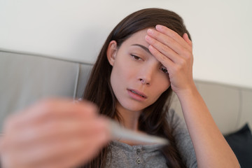 Fototapeta premium Coronavirus fever symptom Asian woman checking high temperature with thermometer. Corona virus infection causes respiratory illness symptoms like cough, headache and in more severe cases, pneumonia.