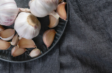 Whole heads and cloves of garlic lie on a metal dish on a gray background. Top view, close-up.