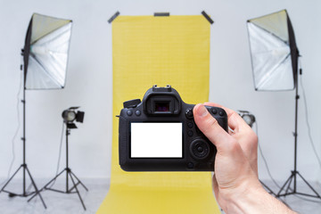Taking photo with camera in a photo studio with yellow backdrop and light equipment