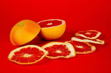 Chips of dried grapefruit sliced in thin circles, shot on a red background. Background for vegetarianism, healthy and wholesome food.