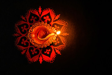 Fototapeta premium A Beautiful terracotta lamp glowing in the dark on a red rangoli with copy space on black background. dhanteras concept