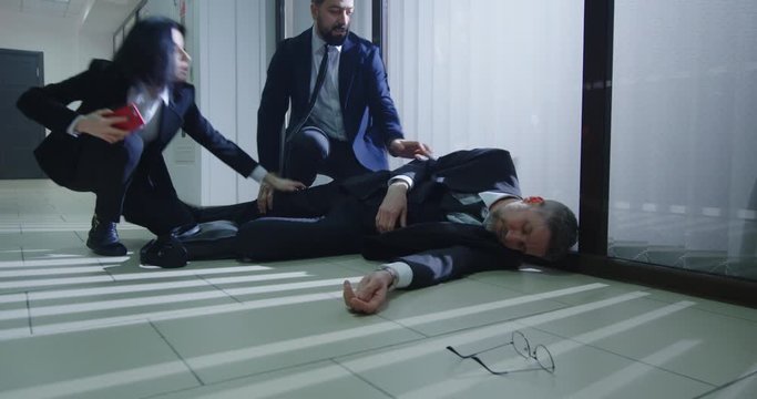 Coworkers helping unconscious manager in office