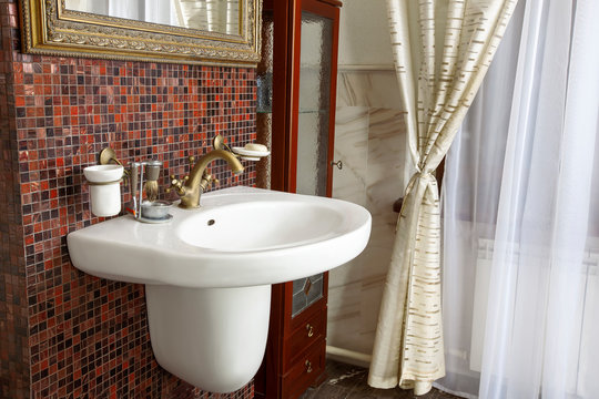 Interior of luxury bathroom in classical style. White sink with bronze faucet, dark red mosaic walls and marble floor, sofisticated design. Indoors, copy space.