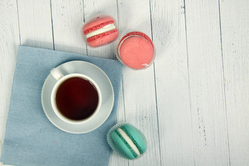 Obraz na płótnie Canvas macaroons of different colours and a cup of tea on a canvas napkin on white wooden background flat lay