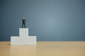 Business conceptual photo – miniature of businessman stands on wooden podium