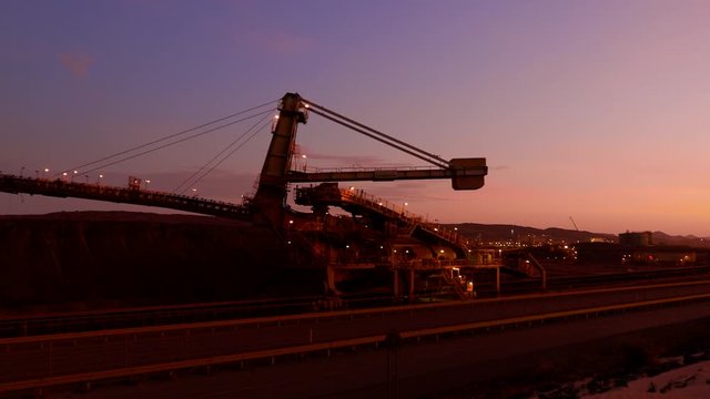 4 K footage of mining industry equipment reclaimer machine, conveyor belts moving raw copper, silver, gold, from train load out stockyard ship load out areas ready to export sunset at the background 