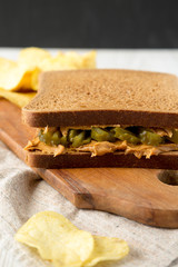 Homemade Peanut Butter Pickle Sandwich with Potato Chips on a rustic wooden board, side view. Close-up.