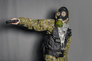 A soldier in camouflage uniform, body armor, in a gas mask with a hood on his head, holds a gun in...