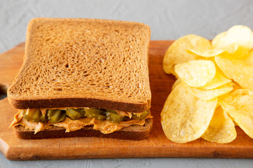 Homemade Peanut Butter Pickle Sandwich with Potato Chips on a rustic wooden board on a gray surface, low angle view. Close-up.