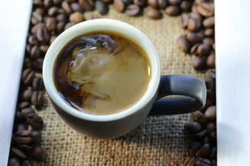 Cup of coffee and coffee grains on burlap. In a wooden frame.