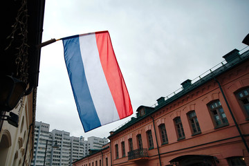 National flag of France on flagpole in front of cloudy sky. French flag on a building on a street of Minsk