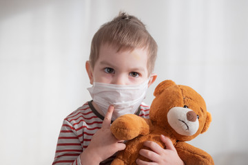 Toddler boy in medical mask embracing his teddy bear. Home isolation coronavirus covid-2019 quarantine