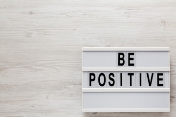 'Be positive' words on a modern board on a white wooden surface, top view. Overhead, from above, flat lay. Copy space.