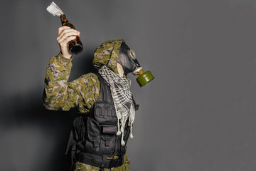 The concept of a terrorist, protesting in a camouflage suit, body armor and gas mask throws Molotov...