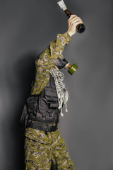 The concept of a terrorist, protesting in a camouflage suit, body armor and gas mask throws Molotov cocktail, incendiary mixture. Studio photo on a gray background.