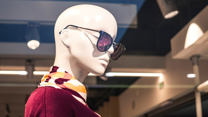 the head of a mannequin in glasses behind a glass shop window. Glare on the glass.