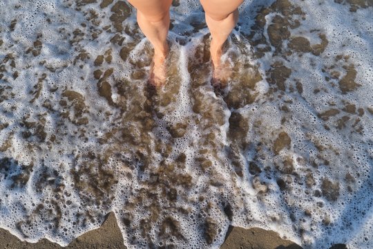 Sea Foamy Wave Washing Woman Bare Feet, Top View