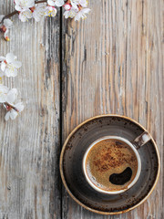 Cup of fresh made coffee and spring branches of white flowers of cherry on a vintage wooden background, top view flat lay.