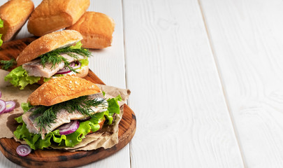 Scandinavian cuisine, seafood burger with freshly baked crispy bun, herring fillet, onions and lettuce. Dish served on a rustic wooden board. Copyspace for text.