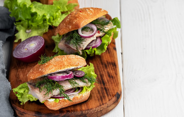 Scandinavian cuisine, seafood burger with freshly baked crispy bun, herring fillet, onions and lettuce. Dish served on a rustic wooden board. Close-up, shallow depth of field.