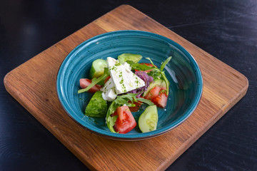 One plate of vegetable salad with feta cheese, cucumbers, tomatoes, and broccoli served in bowl on rustic wooden board.