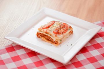 Small piece of tomato lasagna on a square white plate. Dinner in a restaurant, cafe or diner. Healthy food concept.