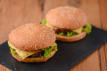 Two hamburgers on the rustic wooden table on black board. Fast food, junk food concept. Food photography concept.