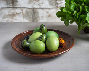 A brown plate with green painted eggs stands on a wooden table