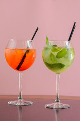Two mojito alcohol cocktails with plastic straw, tropical beverage with ice, mint and lime on pink background copy space