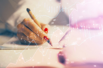 Double exposure of woman's hands making notes with forex graph hologram. Concept stock market...