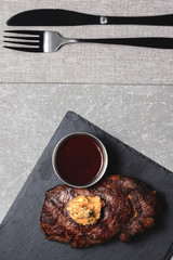 Grilled beef steak medium rare with sauce on black wooden cutting board with utensils. Copy space, flat lay.