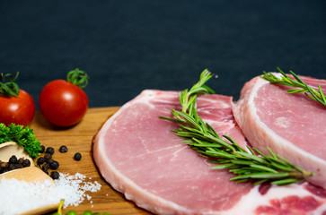Raw pork chop meat on wood plate with vegetables, spices, salt and black pepper in dark black cloth table