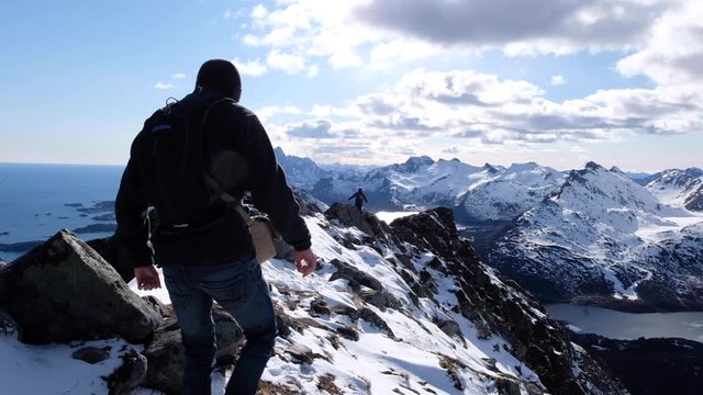 Hiker walking across Svolvaergeita mountain summit in winter, Lofoten, Norway