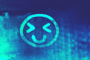Blue happy smile face with eyes narrowed painted on dirty window flooded with raindrops on blur glass blue background in city