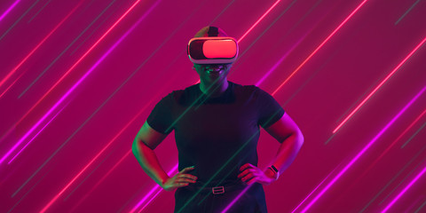 Creative emotions and neon lines on pink background, flyer, proposal. African-american young woman in VR set. Concept of human emotions, facial expression, sales, ad, inclusion, diversity. Modern art.