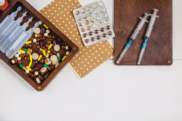 An open wooden box with medicines on a white background. Next to it is a band- aid, an open plate with tablets and syringes. Space for text. The concept of viral infection.