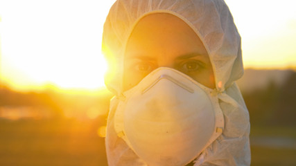 PORTRAIT: Female doctor wearing a facemask and suit stands outside in sunset