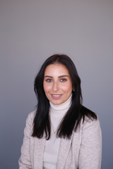 Portrait of a smiling mid-aged business woman in a light milk-colored trouser suit and turtleneck against a light wall.