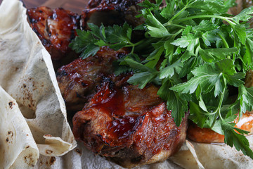 Board on which stands a dish of meat. Chicken legs, fried pork, sausages, all in pita bread. Parsley. Mustard with ketchup in cups. On a dark background.