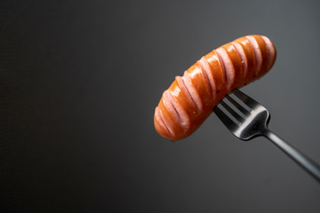 Fork with fried sausage on a grey background