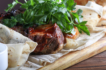 Board on which stands a dish of meat. Chicken legs, fried pork, sausages, all in pita bread. Parsley. Mustard with ketchup in cups. On a dark background.