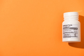Top view of white container with dietary supplements on orange background