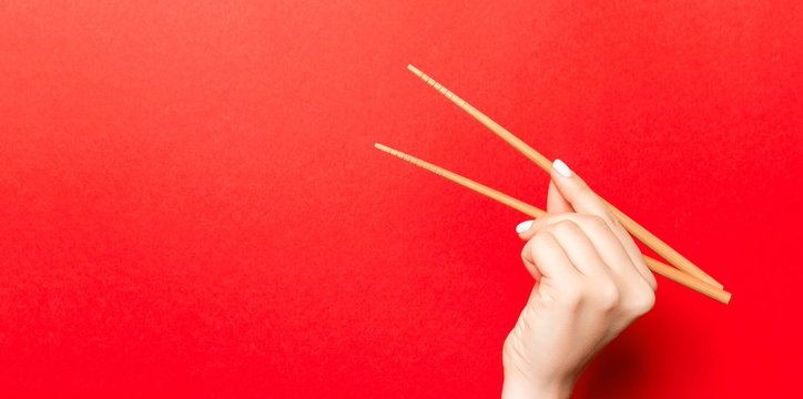 Creative image of wooden chopsticks in female hand on red background. Japanese and chinese food with copy space