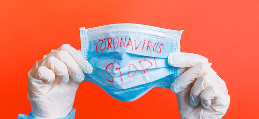 Female hands in medical gloves holding protective mask with stop coronavirus text on it at red background. Health care concept. Coronavirus concept