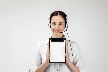 Beautiful smiling woman consultant of call center in headphones holding clipboard with blank white...
