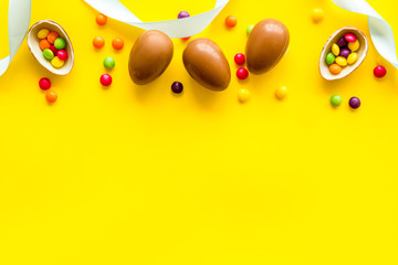 Easter background with chocolate eggs and dragees on yellow background top-down frame copy space