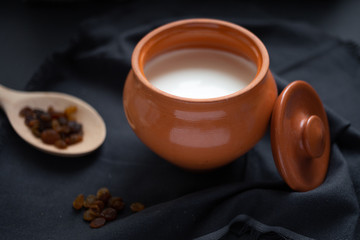 Brown pot with sour cream and a wooden spoon with raisins on a dark background.